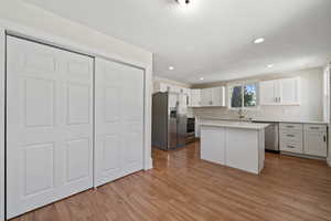 Kitchen featuring white cabinets, sink, light wood-type flooring, appliances with stainless steel finishes, and a kitchen island