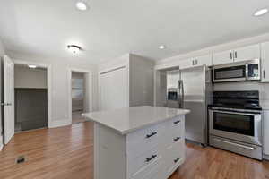 Kitchen featuring a center island, light hardwood / wood-style flooring, light stone countertops, appliances with stainless steel finishes, and white cabinetry