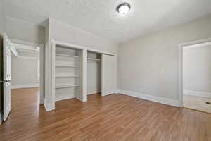 Unfurnished bedroom featuring two closets, a textured ceiling, and light hardwood / wood-style floors