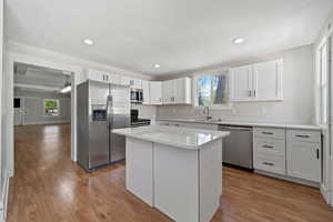 Kitchen with white cabinets, sink, light stone countertops, appliances with stainless steel finishes, and a kitchen island