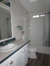 Full bathroom with shower / bath combo, vanity, vaulted ceiling, hardwood / wood-style flooring, and toilet