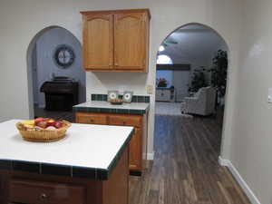 Kitchen looking into living room area featuring tile edged counters, dark hardwood / wood-style flooring, a kitchen island, and lofted ceiling