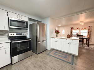 Kitchen featuring backsplash, light wood-type flooring, white cabinetry, kitchen peninsula, and stainless steel appliances