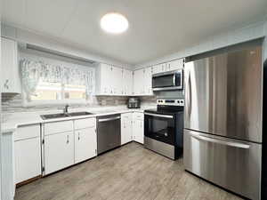 Kitchen featuring tasteful backsplash, white cabinetry, sink, and stainless steel appliances