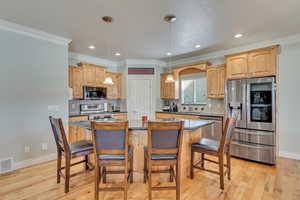 Kitchen with a kitchen breakfast bar, crown molding, light wood-type flooring, appliances with stainless steel finishes, and a kitchen island