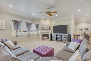 Carpeted living room with a fireplace, ceiling fan, and crown molding