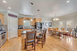 Kitchen with tasteful backsplash, ornamental molding, stainless steel appliances, decorative light fixtures, and a center island that seats 6 chairs.