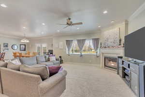 Living room with ceiling fan with notable chandelier, plenty of natural light, crown molding, and a tiled fireplace