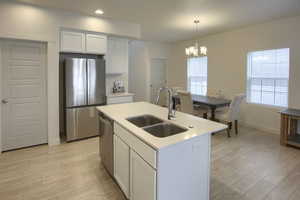 Kitchen featuring sink, hanging light fixtures, an island with sink, white cabinets, and appliances with stainless steel finishes