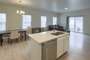 Kitchen with a kitchen island with sink, sink, dishwasher, white cabinetry, and hanging light fixtures