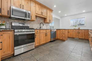 Kitchen with light stone countertops, appliances with stainless steel finishes, decorative backsplash, and sink