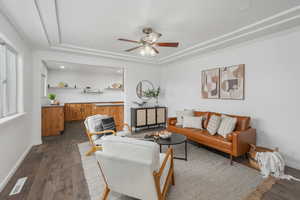 Living room with ornamental molding, a raised ceiling, ceiling fan, and dark wood-type flooring