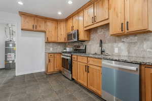 Kitchen with backsplash, stainless steel appliances, light stone counters, and water heater