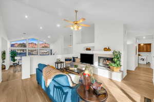 Living room with ceiling fan, light hardwood / wood-style floors, a tile fireplace, and vaulted ceiling