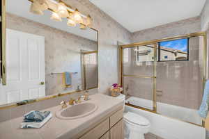 Full bathroom featuring vanity, toilet, and bath / shower combo with glass door