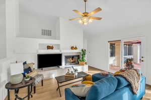 Living room featuring a tiled fireplace, ceiling fan, light hardwood / wood-style floors, and vaulted ceiling