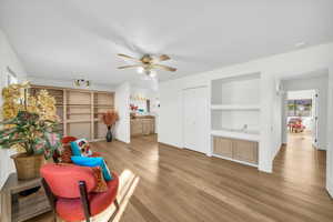 Sitting room with built in shelves, ceiling fan, and light hardwood / wood-style flooring