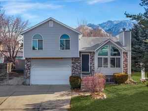 Tri-level home with a mountain view, a garage, and a front lawn- grass is edited green.