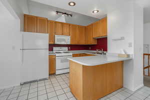 Kitchen with kitchen peninsula, white appliances, light tile patterned flooring, and sink