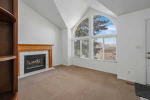 Unfurnished living room featuring light colored carpet, lofted ceiling, and a tile fireplace