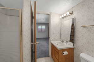 Bathroom featuring vanity, a textured ceiling, and toilet-access from both bedrooms downstairs.