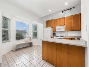 Kitchen with lofted ceiling, white appliances, track lighting, light tile patterned flooring, and kitchen peninsula