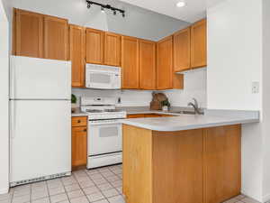 Kitchen with light tile patterned flooring, white appliances, kitchen peninsula, and sink