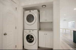 Laundry area featuring a notable chandelier, stacked washer / drying machine, cabinets, and light hardwood / wood-style flooring