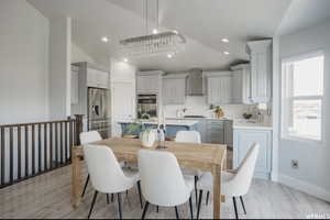 Dining space with sink, light hardwood / wood-style floors, vaulted ceiling, and an inviting chandelier