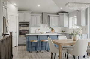 Kitchen with gray cabinetry, lofted ceiling, wall chimney range hood, and appliances with stainless steel finishes