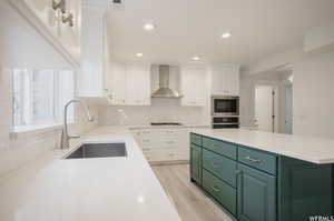 Kitchen with wall chimney range hood, sink, light hardwood / wood-style flooring, built in microwave, and white cabinetry