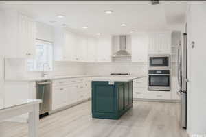 Kitchen with white cabinets, sink, wall chimney exhaust hood, light wood-type flooring, and appliances with stainless steel finishes