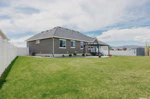 Rear view of house featuring a pergola, central AC, a storage unit, and a lawn