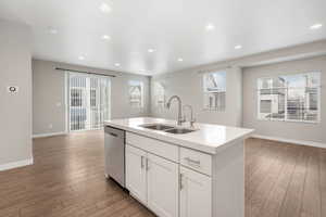 Kitchen featuring stainless steel dishwasher, a kitchen island with sink, sink, light hardwood / wood-style floors, and white cabinetry