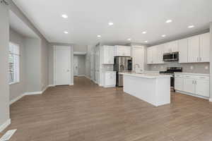 Kitchen with sink, an island with sink, appliances with stainless steel finishes, light hardwood / wood-style floors, and white cabinetry