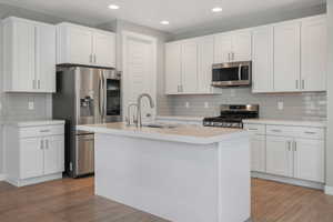 Kitchen featuring a kitchen island with sink, sink, light hardwood / wood-style flooring, white cabinetry, and stainless steel appliances