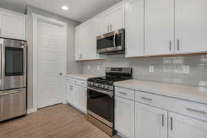 Kitchen featuring white cabinets, decorative backsplash, light wood-type flooring, light stone countertops, and appliances with stainless steel finishes