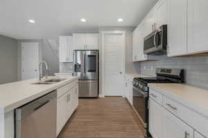 Kitchen with sink, stainless steel appliances, light hardwood / wood-style flooring, backsplash, and white cabinets