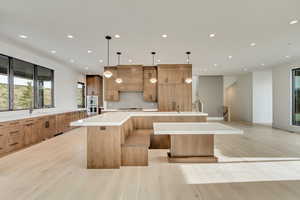 Kitchen with a breakfast bar, white double oven, premium range hood, hanging light fixtures, and a large island