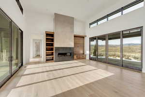 Unfurnished living room with a multi sided fireplace, a mountain view, a towering ceiling, and light hardwood / wood-style floors