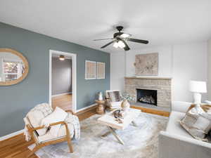 Living room featuring hardwood / wood floors, a stone fireplace, and ceiling fan