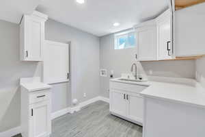 Clothes washing area with electric dryer hookup, cabinets, sink, light hardwood / wood-style flooring, and washer hookup