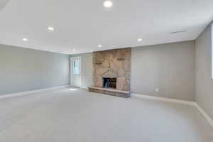 Unfurnished living room featuring a stone fireplace and light carpet