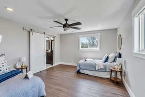 Bedroom with a barn door, ensuite bath, ceiling fan, and dark wood-type flooring