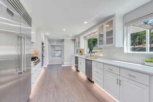 Kitchen with sink, stainless steel appliances, decorative backsplash, white cabinets, and hardwood / wood-style flooring