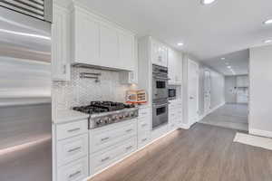 Kitchen with light stone countertops, backsplash, stainless steel appliances, white cabinets, and dark hardwood / wood-style floors