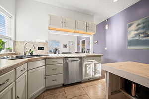 Kitchen with white cabinetry, sink, stainless steel dishwasher, plenty of natural light, and a textured ceiling