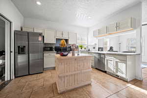 Kitchen featuring a textured ceiling, a kitchen island, black appliances, light tile patterned floors, and white cabinetry