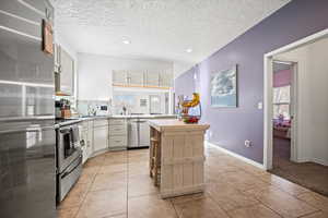 Kitchen with appliances with stainless steel finishes, light tile patterned floors, a textured ceiling, and white cabinetry