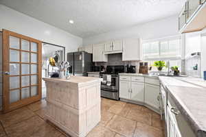 Kitchen with sink, stainless steel appliances, light tile patterned floors, backsplash, and white cabinets